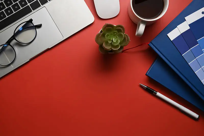 Mesa de trabajo con portátil, gafas, café y cuaderno de un desarrollador web en Castellón